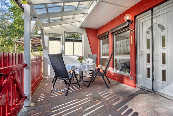 A covered patio with a table and chairs, a red fence, and a building with a number 19 sign.