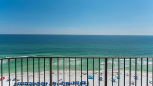 A beach view from a balcony with a railing, clear blue sky, and calm sea.