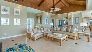 A spacious living room with a high ceiling, wooden beams, and a large ceiling fan.