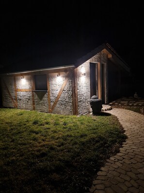 A stone building with a wooden door and windows, illuminated by exterior lights.