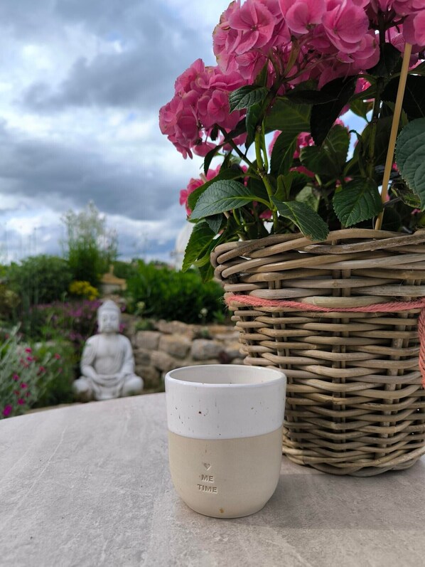A white ceramic mug with 'ME TIME' inscribed, placed on a stone surface next to a wicker basket with pink flowers.