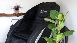 Una silla de masaje con panel de control, una planta en maceta y un pequeño estante con una flor y una tarjeta.