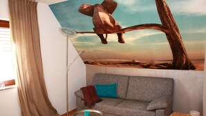 Una habitación con sofá, una mesita auxiliar, una lámpara de pie y un mural grande con un elefante sobre una rama de árbol.