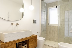 A bathroom with a large mirror, a wooden vanity, a toilet, a glass shower enclosure, and a bidet.