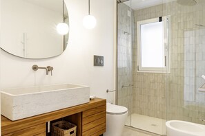 A bathroom with a large mirror, a wooden vanity, a toilet, a glass shower enclosure, and a bidet.