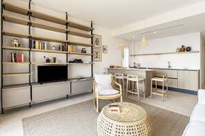 A modern living room with a TV, bookshelves, a dining area, and a kitchen.