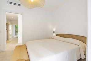 Une chambre à coucher comprenant un lit, un banc, une lampe fixée au mur et une porte donnant sur un balcon.