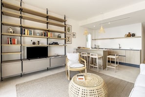 A modern living room with a TV, bookshelves, a dining area, and a kitchen.