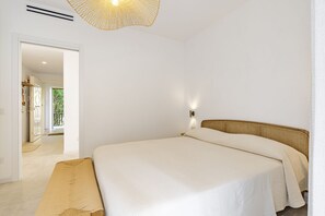 A bedroom with a bed, a bench, a wall-mounted light, and a door leading to a balcony.