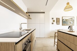 Une cuisine moderne dotée d’un îlot central, d’un four encastré et d’un luminaire suspendu.