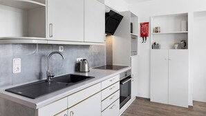 A modern kitchen with white cabinetry, a stainless steel sink, a built-in oven, and a flat-screen TV mounted above the oven. - Room 'Gästezimmer 1 Mit Bad' with Shared Terrace, Wi-Fi and Air Conditioning (Wartenberg)