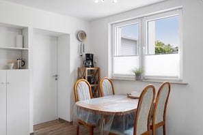 A compact kitchen with a dining area, a coffee machine, and a window with blinds.