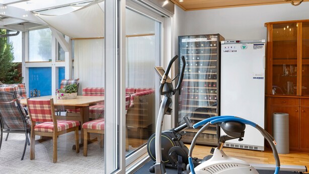 A room with a glass door leading to an outdoor area, a treadmill, a refrigerator, and a wooden cabinet. - Room 'Gästezimmer 1 Mit Bad' with Shared Terrace, Wi-Fi and Air Conditioning (Wartenberg)