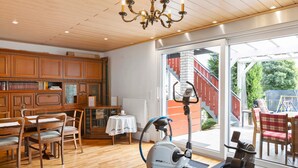 A room with a wooden floor, a ceiling with recessed lighting, a chandelier, a treadmill, and a dining area with chairs and a table. - Room 'Gästezimmer 1 Mit Bad' with Shared Terrace, Wi-Fi and Air Conditioning (Wartenberg)