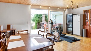 A spacious room with a wooden dining table, chairs, a treadmill, and a refrigerator. - Room 'Gästezimmer 1 Mit Bad' with Shared Terrace, Wi-Fi and Air Conditioning (Wartenberg)