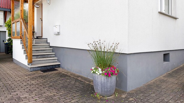 A building with a staircase, a large planter with flowers, and a window. - Room 'Ruhiges Zimmer 2' with Shared Terrace, Wi-Fi and Air Conditioning (Wartenberg)