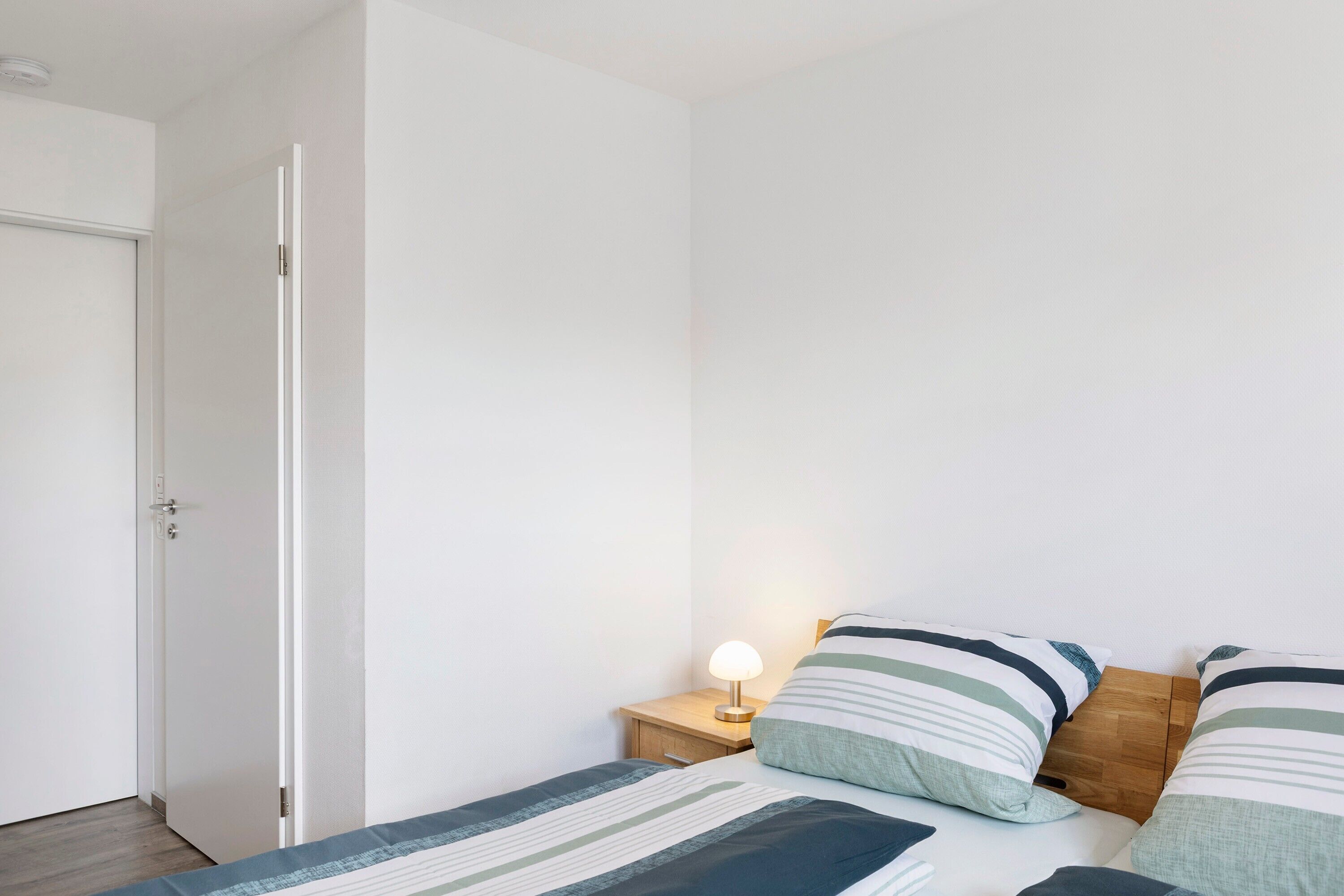 Un dormitorio con una cama, una mesita de noche con una lámpara y una mesita auxiliar de madera.