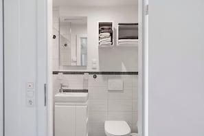 A modern bathroom with a white sink, toilet, and a mirror above the sink. There are two towel racks with folded towels.