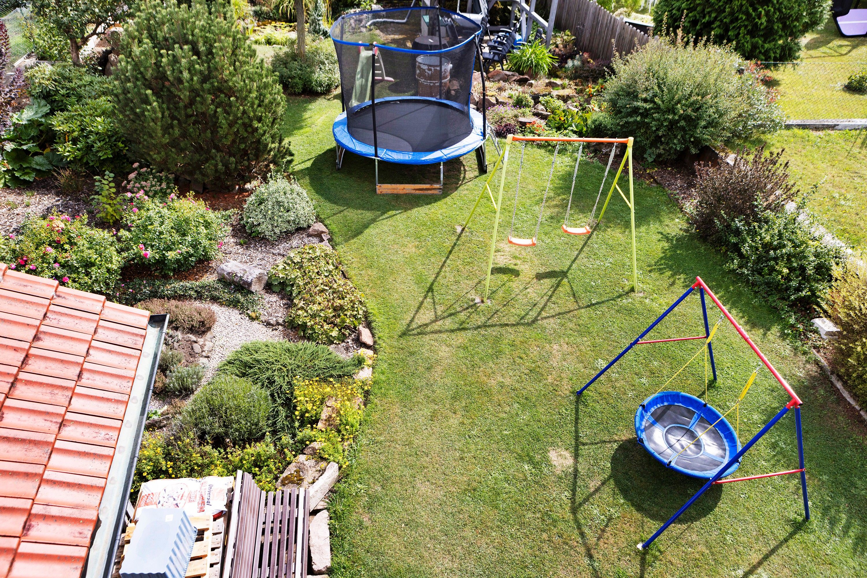 A backyard with a trampoline, swing set, and a small garden area.
