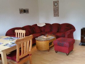 A living room with a red sofa, a wooden chair, a wicker coffee table, and a small ottoman.