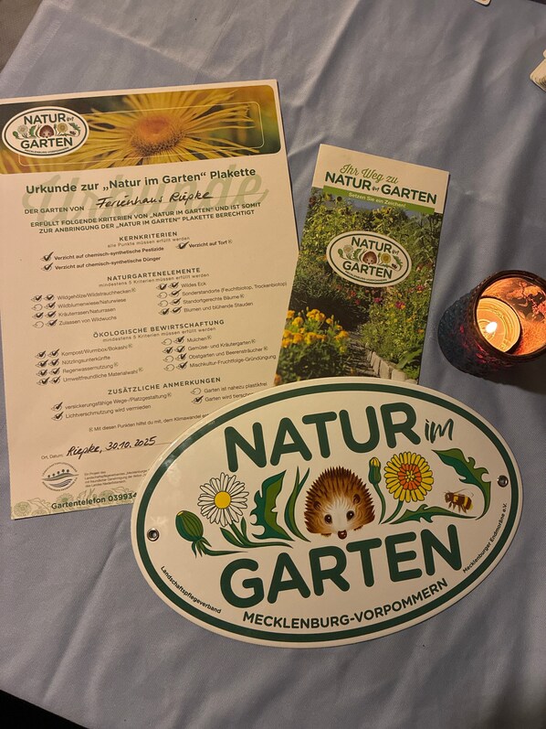 Une table avec un set de table orné d’un logo et d’un texte relatifs à « Natur im Garten » (la nature dans le jardin), une bougie et un livret.