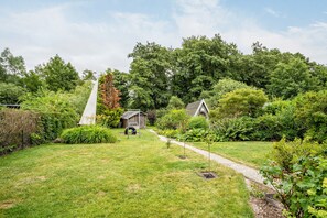 Um jardim bem cuidado, com gramado, um pequeno galpão de madeira e uma área de recreação com baloiço.