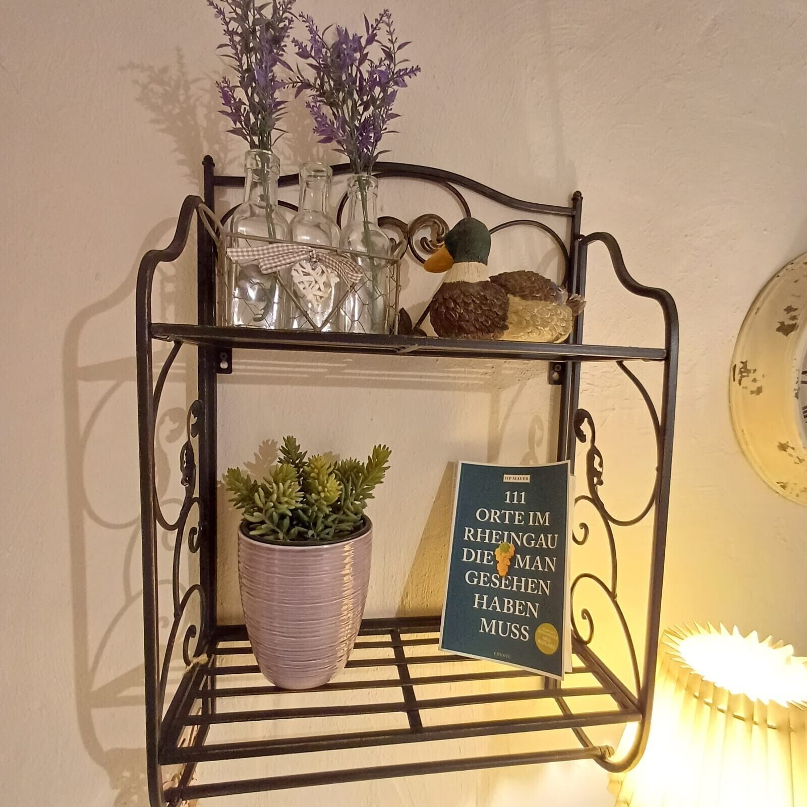 Een metalen schap met decoratieve objecten, waaronder een potplant, een beeldje van een eend en een ingelijst boek.