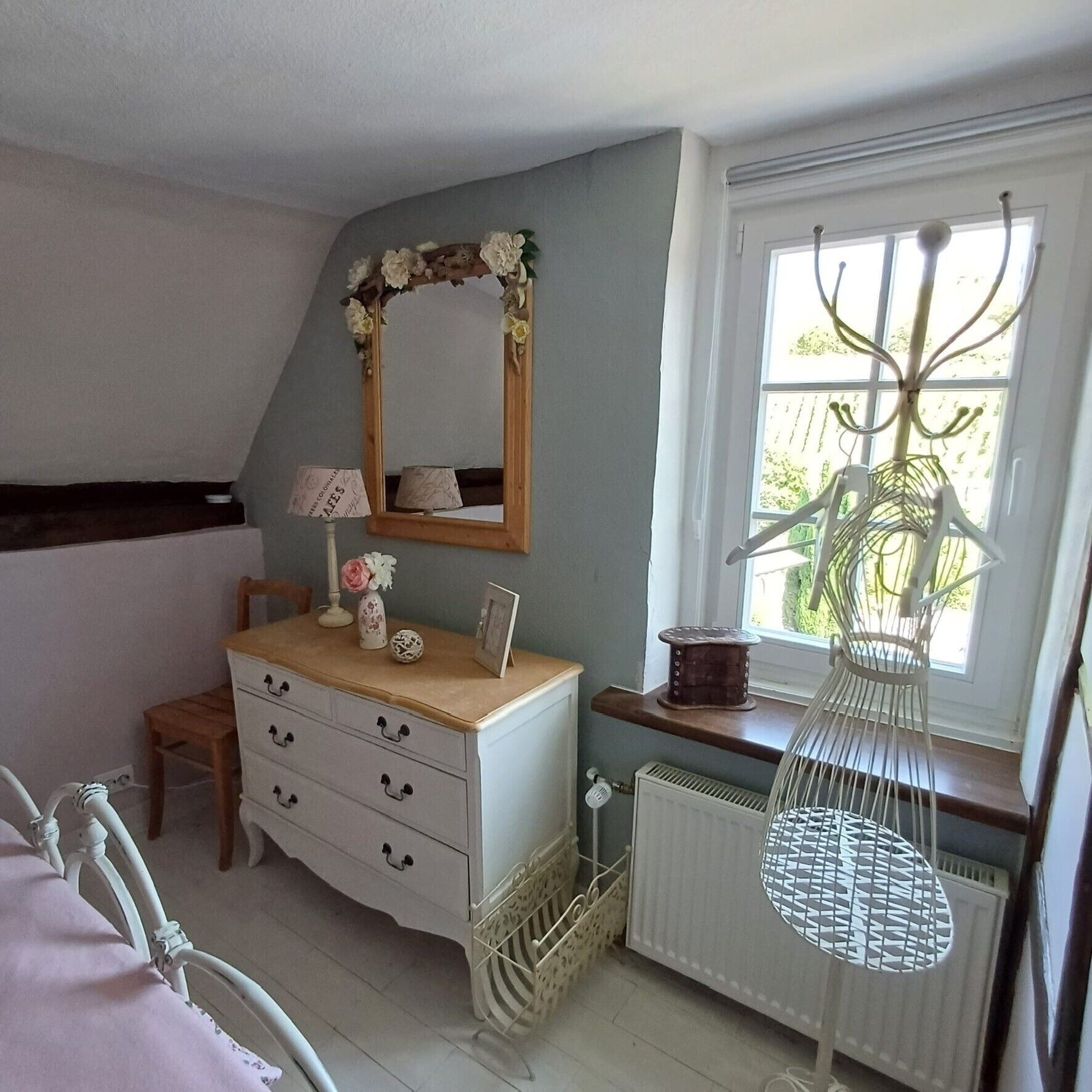A bedroom with a dresser, a mirror, a radiator, a window with a plant, and a bed.