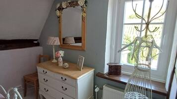 A bedroom with a dresser, a mirror, a radiator, a window with a plant, and a bed.