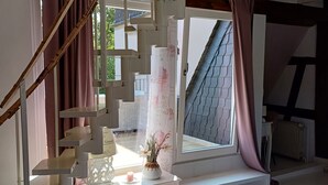 A bedroom with a staircase, a window with curtains, a bedside table with a lamp, and a bed with a quilted cover. - Apartment 'Weinbergsblick' with Private Terrace, Private Garden and Balcony (Geisenheim)