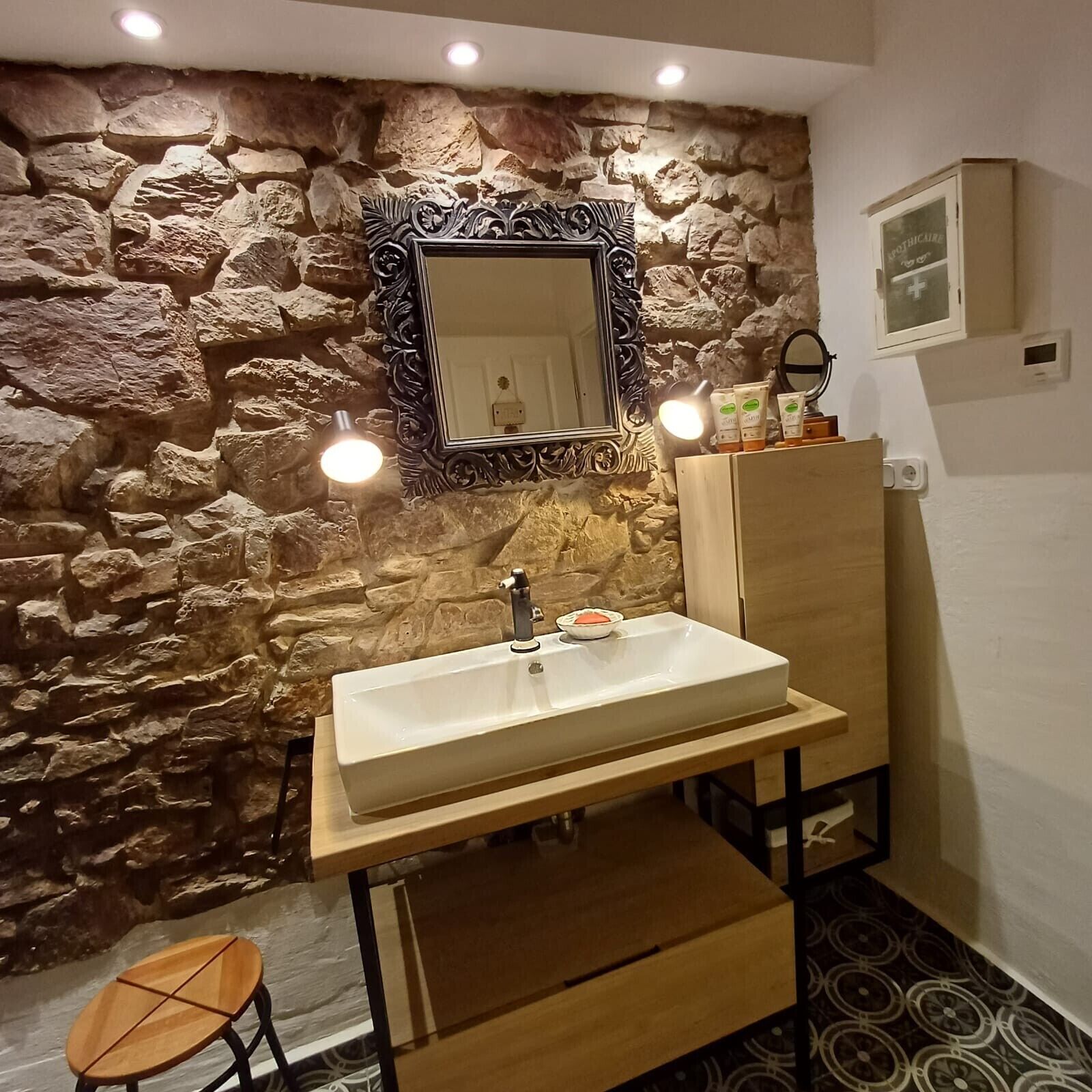 A bathroom with a stone wall, a large mirror, a sink, and a vanity.