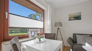 A room with a table, chairs, a sofa, a lamp, a painting, and a window with blinds.