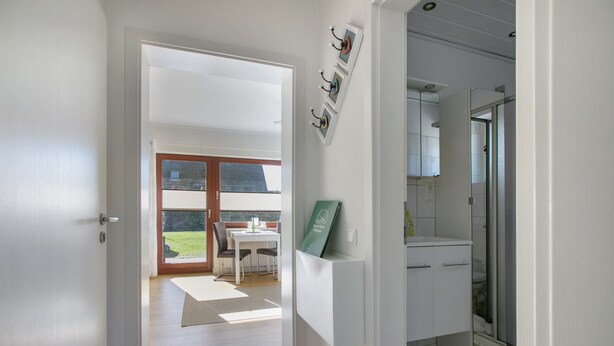 A hallway leading to a dining area with a view of the outdoors, a kitchen with a sink and cabinets, and a door to a bathroom.
