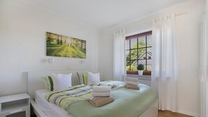 A bedroom with a bed, a nightstand, a window with curtains, and a painting on the wall.