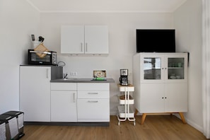Une cuisine compacte avec des meubles blancs, un four à micro-ondes, une machine à café et un téléviseur posé sur un meuble.