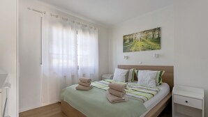 A bedroom with a bed, a nightstand, a painting, and a window with curtains.