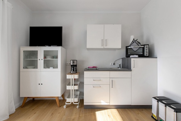 A compact kitchen with white cabinets, a microwave, a coffee maker, and a TV on a cabinet.