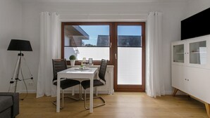 A dining area with a table and chairs, a lamp, a cabinet, and a view through a glass door.