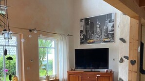 Una sala de estar acogedora con televisor, muebles de madera, una mesa redonda y un ventanal grande.