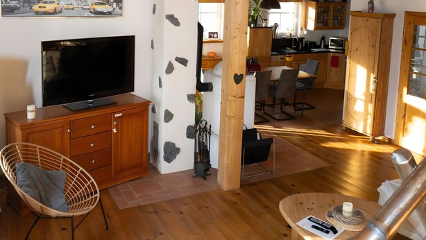 Un espacio habitable amplio con televisor, muebles de madera, una mesa de comedor y una escalera que sube a un nivel superior.
