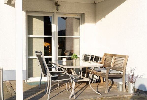 A patio with a table and chairs, a potted plant, and a metal bucket. - Holiday Home 'Das Blaue Haus Am Rothaarsteig' with Private Terrace, Private Garden and Wi-Fi (Kirchhundem)