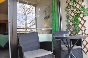 Un balcone con sedie in vimini, un tavolino rotondo e un muro decorativo con piante.