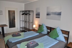 A room with two beds, a wardrobe, a desk, and a lamp.