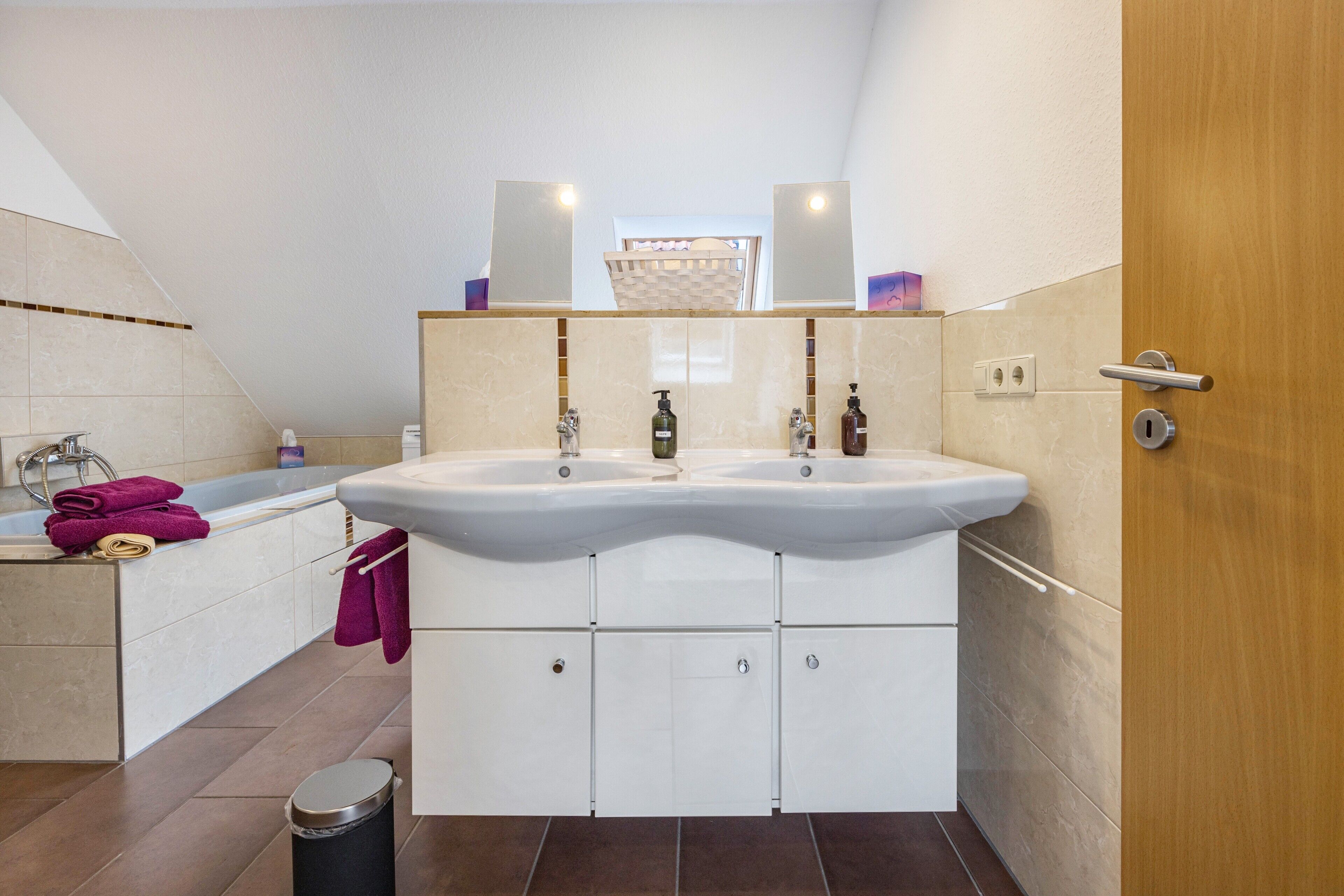 Un baño con lavamanos doble, bañera y puerta de madera.