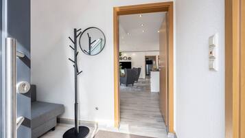 Ein modernes Interieur mit einem grauen Sofa, einem Kleiderständer und einer Holztür, die in einen Wohnbereich führt.