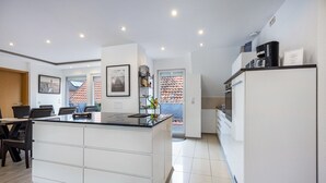 Une cuisine moderne dotée d’un îlot central, de meubles blancs et d’un coin repas avec des chaises.