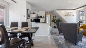 Une cuisine moderne avec un coin repas, un salon doté d’un canapé et un escalier menant à un niveau supérieur.