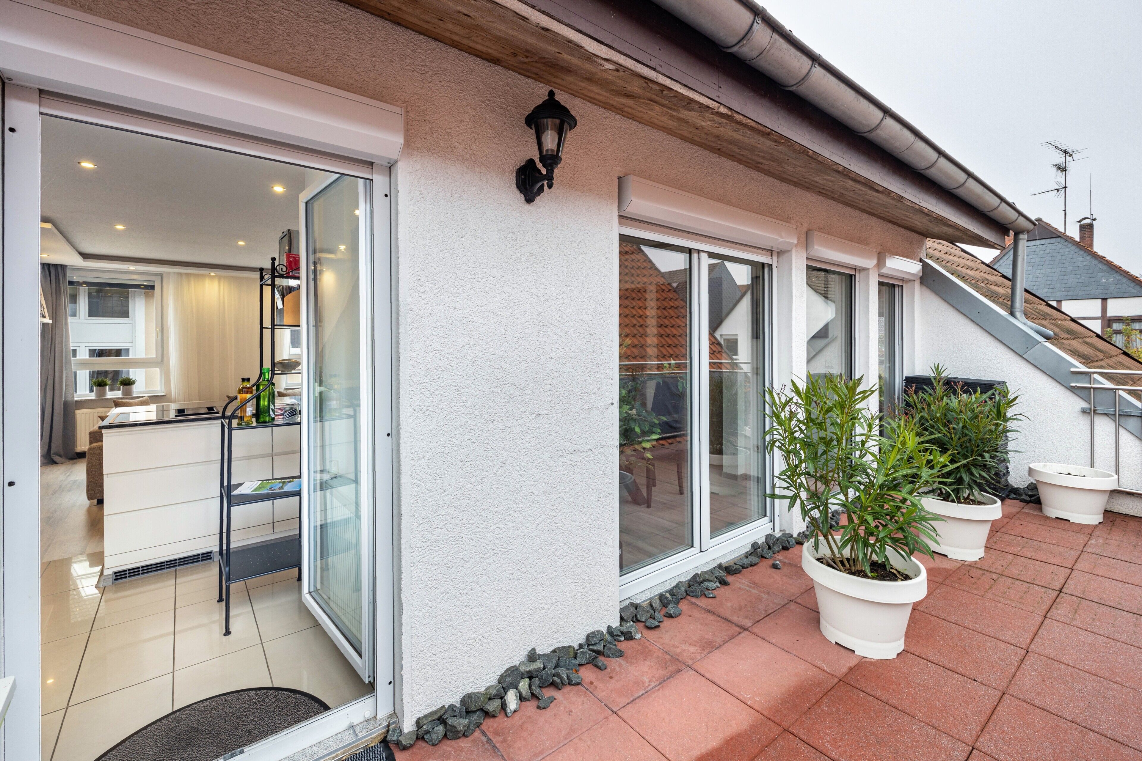 A modern house with a glass door entrance, a kitchen with white cabinets, and potted plants on the patio.