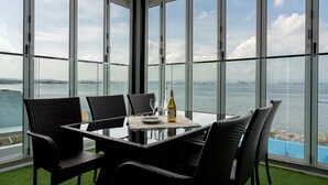 Un balcone con un tavolo in vetro, quattro sedie in vimini, una bottiglia di vino e vista sull'acqua e sulla città in lontananza.