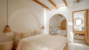 Camera da letto con un letto grande, soffitto in legno, uno specchio rotondo e bagno con lavandino e specchio.